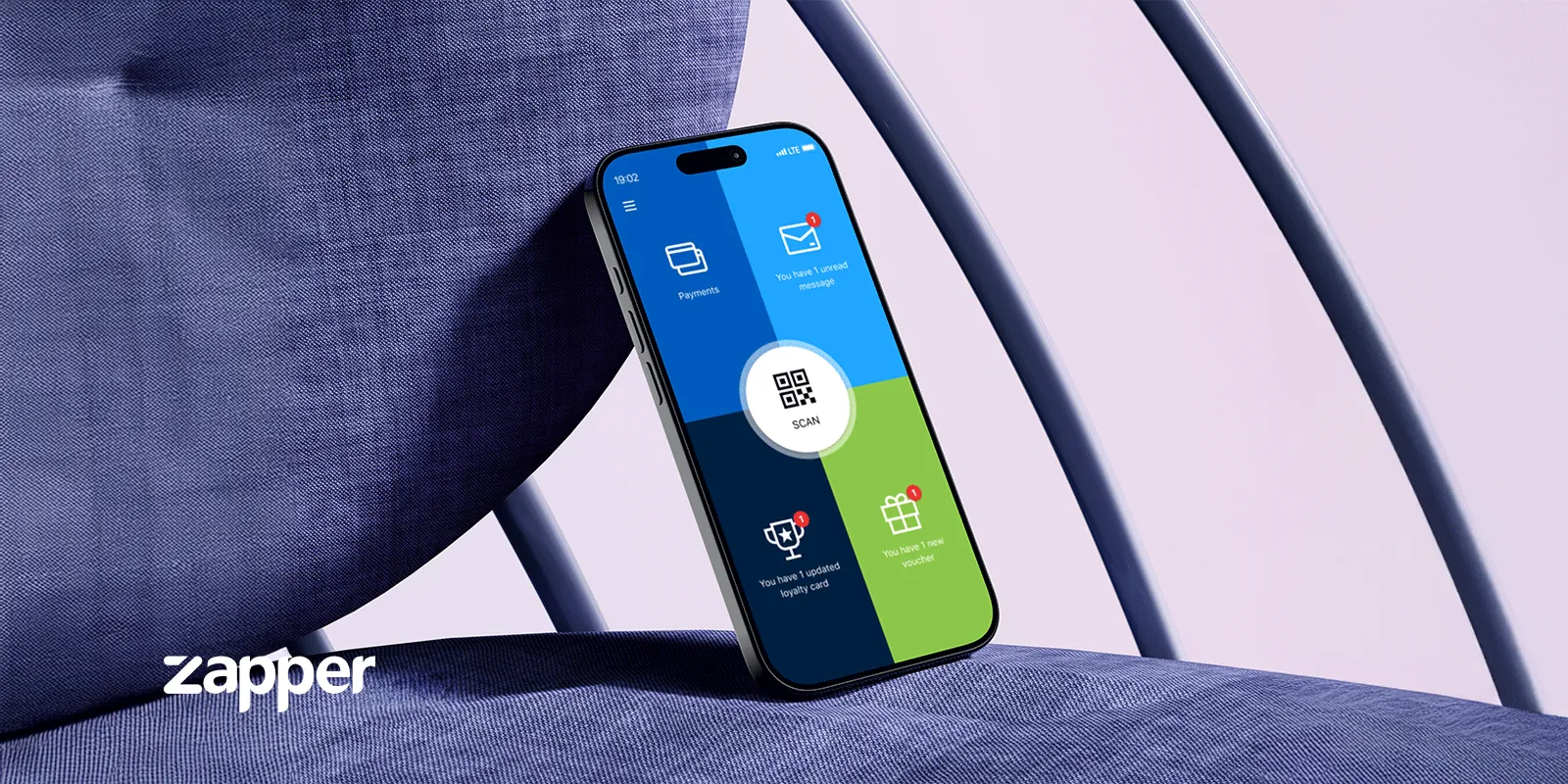 Zapper app home screen with Payments, Scan, messages, loyalty card and voucher tiles, on a phone resting on a blue chair